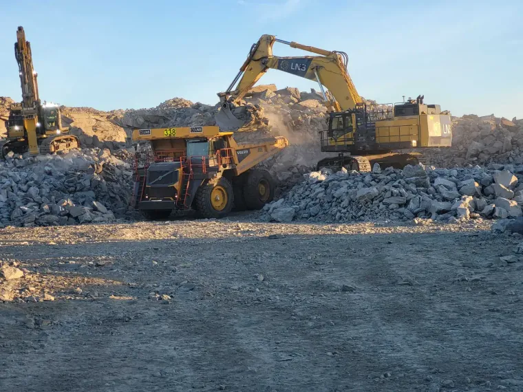 Gravemaskin laster en dumper på et masseuttak